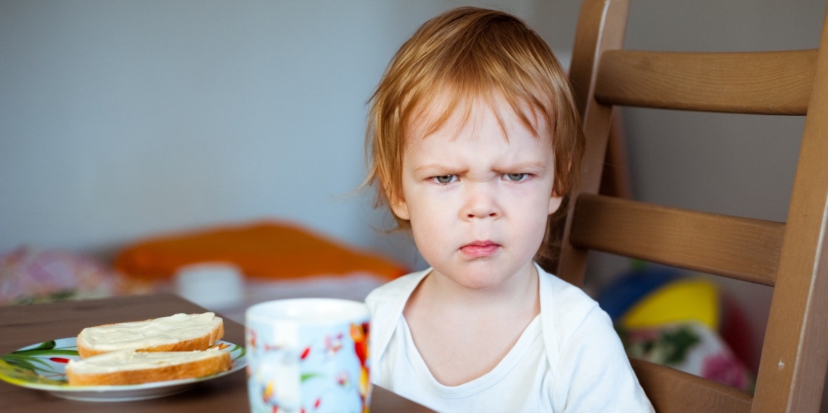 angry child with sandwich and cup on the table