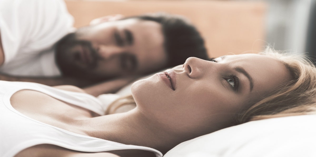 worried woman laying in bed next to man