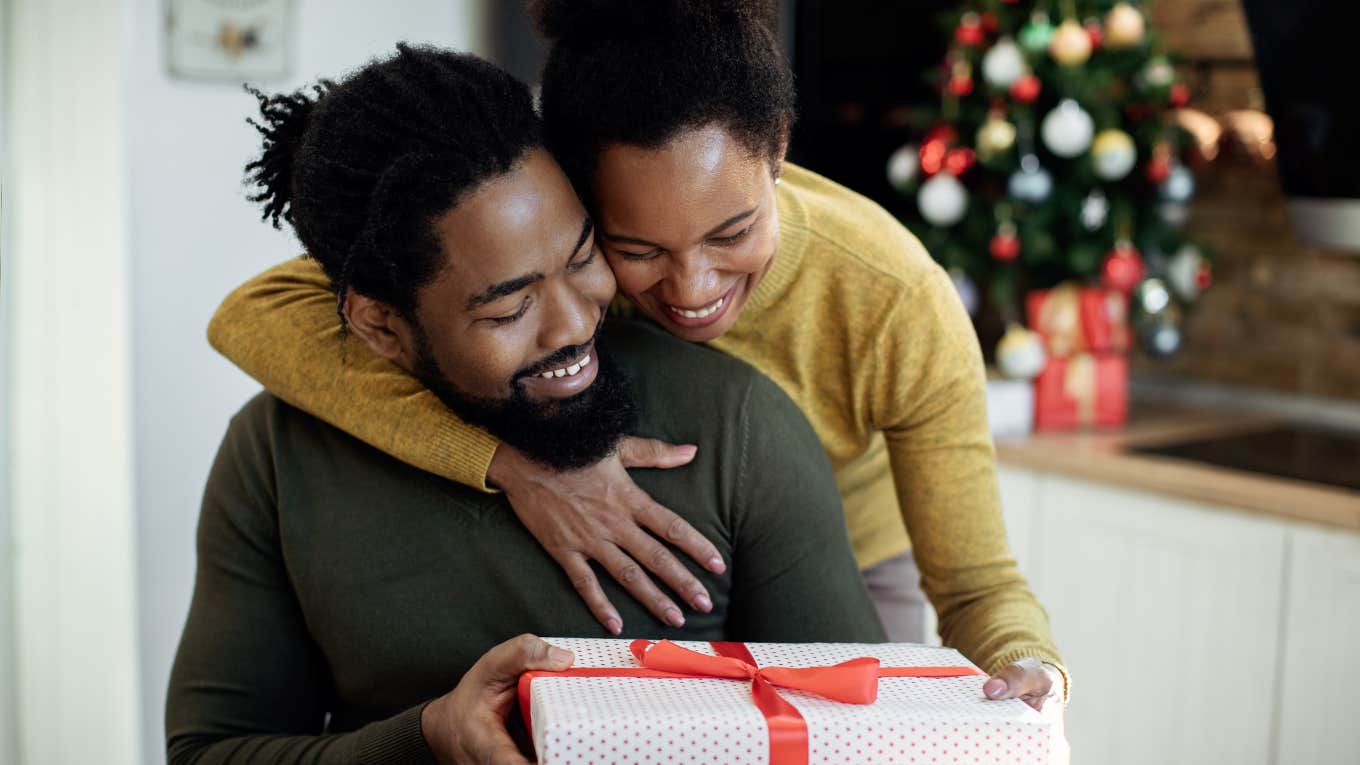 woman embracing her husband and giving his a gift on Christmas day at home.