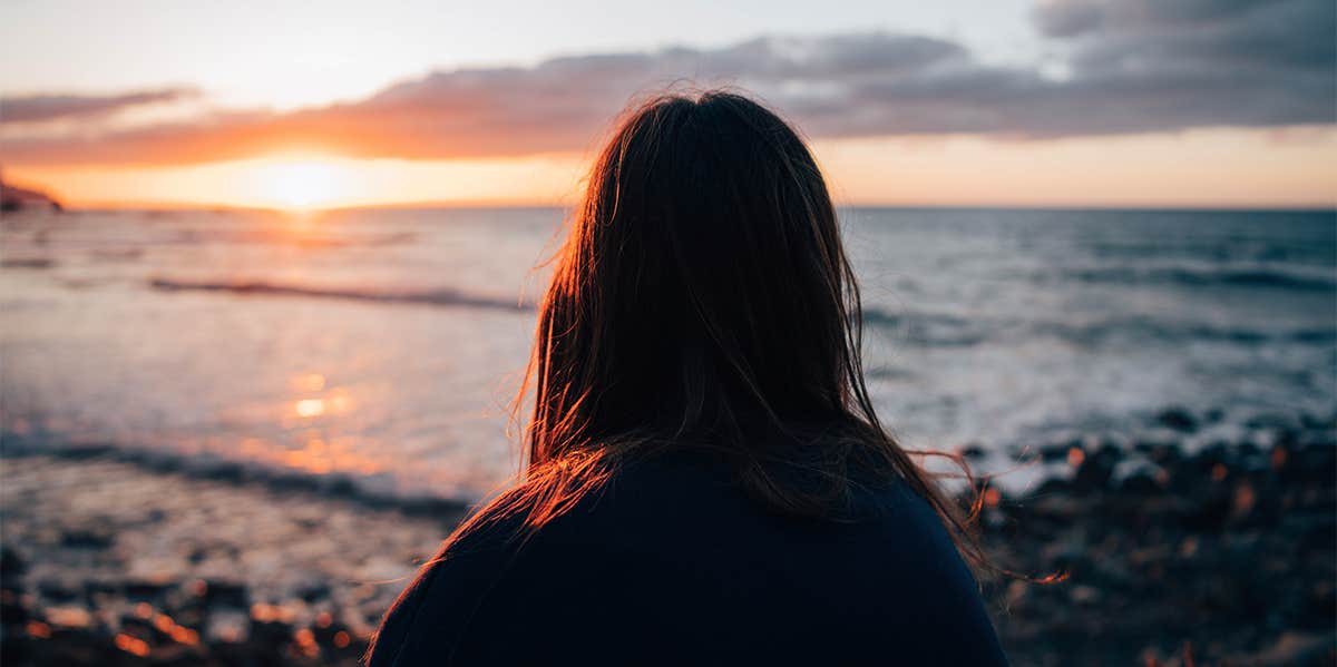 girl sitting alone at beach watching sunset