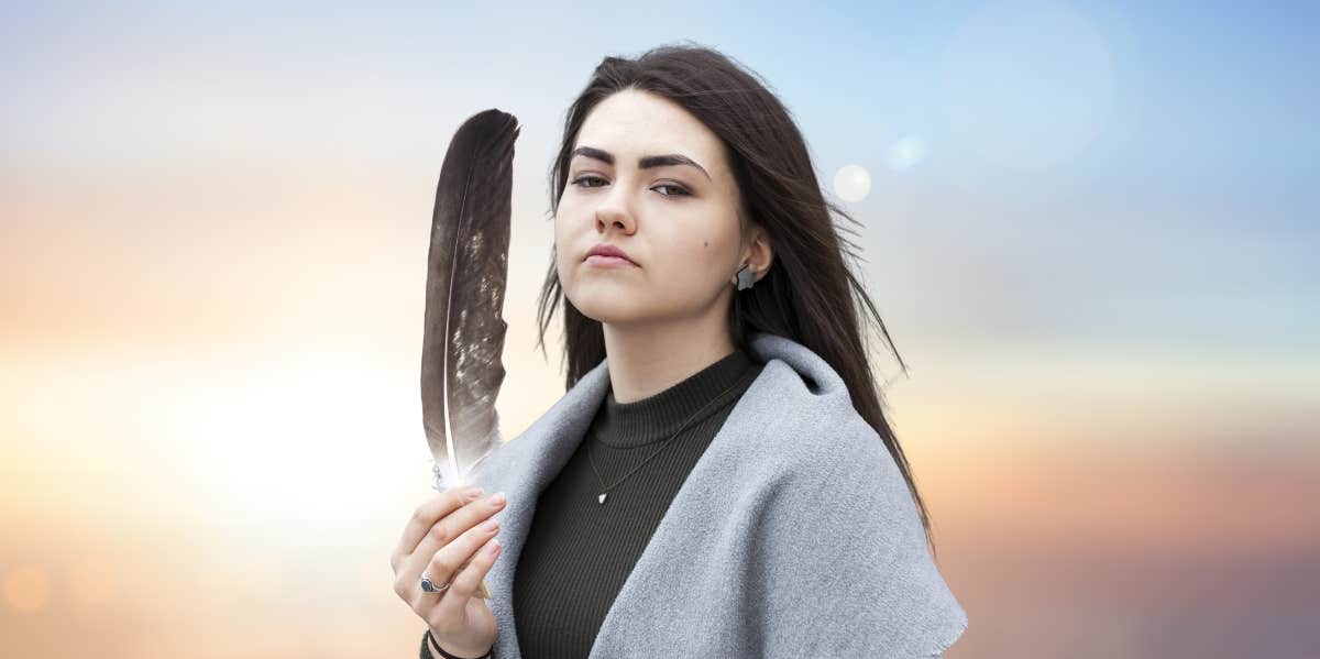 woman holding up a gray feather