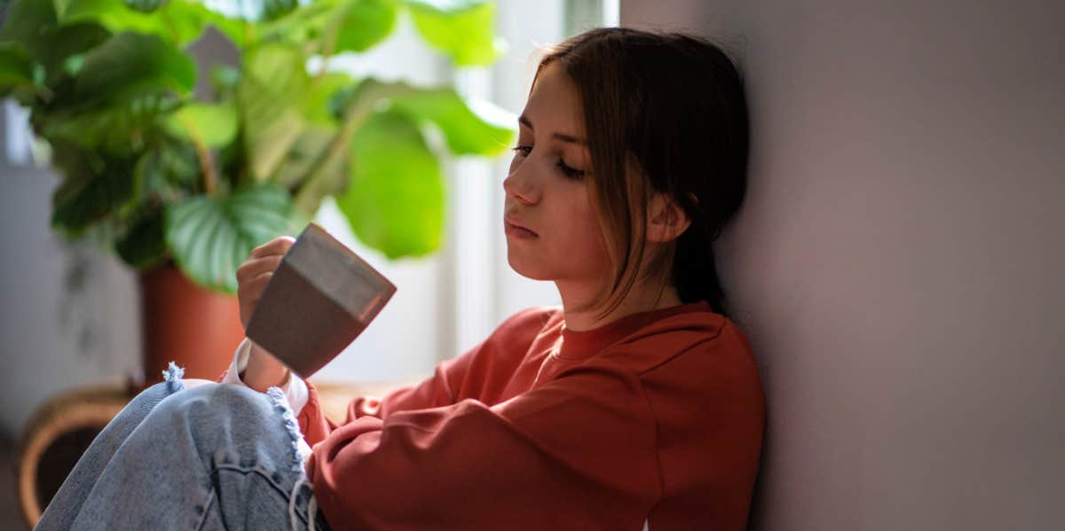 woman drinking coffee sitting near window unhappy