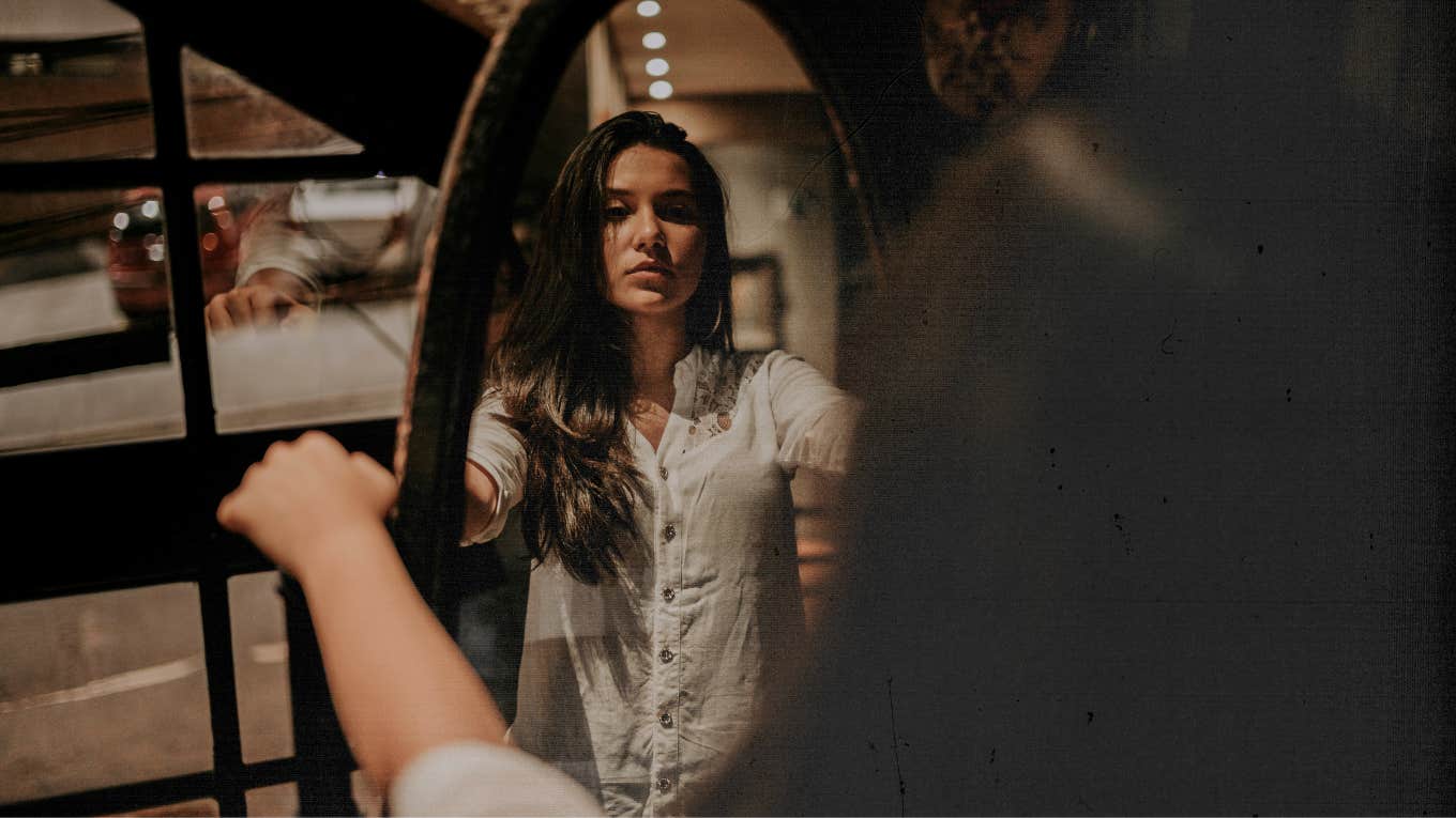 Woman grasping the sides of the mirror, looking at herself