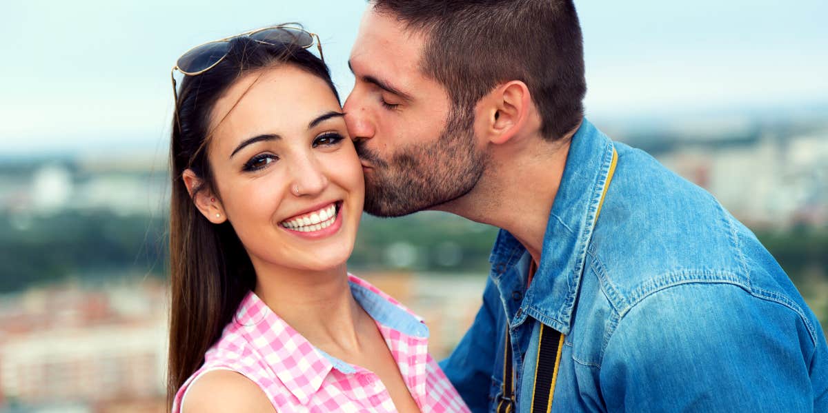 woman smiling while being kissed on the cheek by a man who loves her