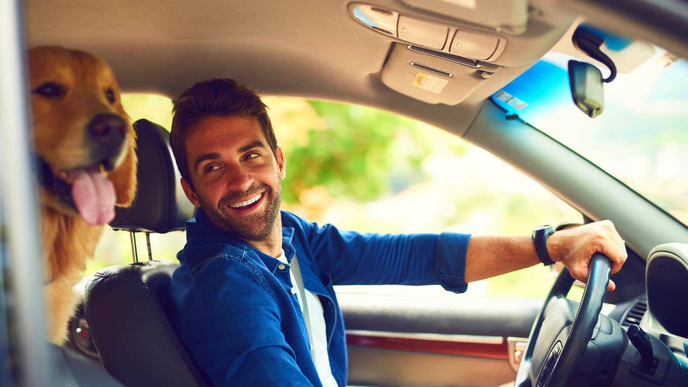 smiling man driving in his car with his dog