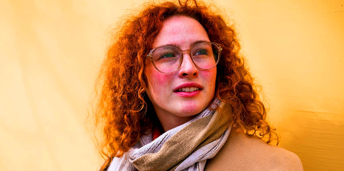 woman with red hair and glasses standing against wall
