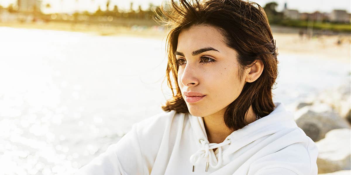 young woman sitting thoughtfully by a lake, thinking deeply