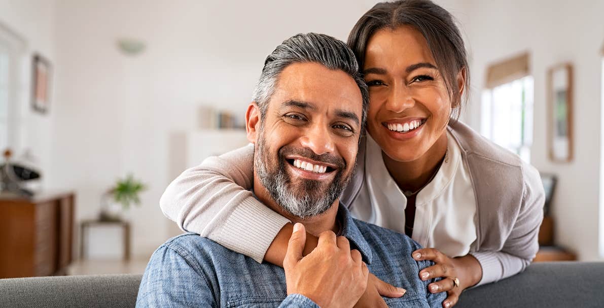 couple embracing and looking at camera sitting on sofa.