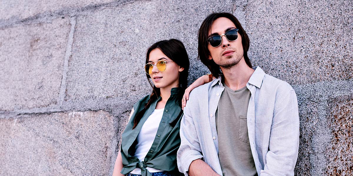 couple standing against a brick wall, man looking at camera