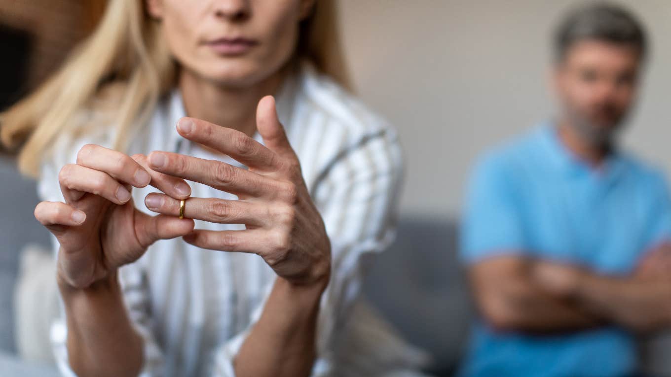 Woman taking her ring off with husband in the background