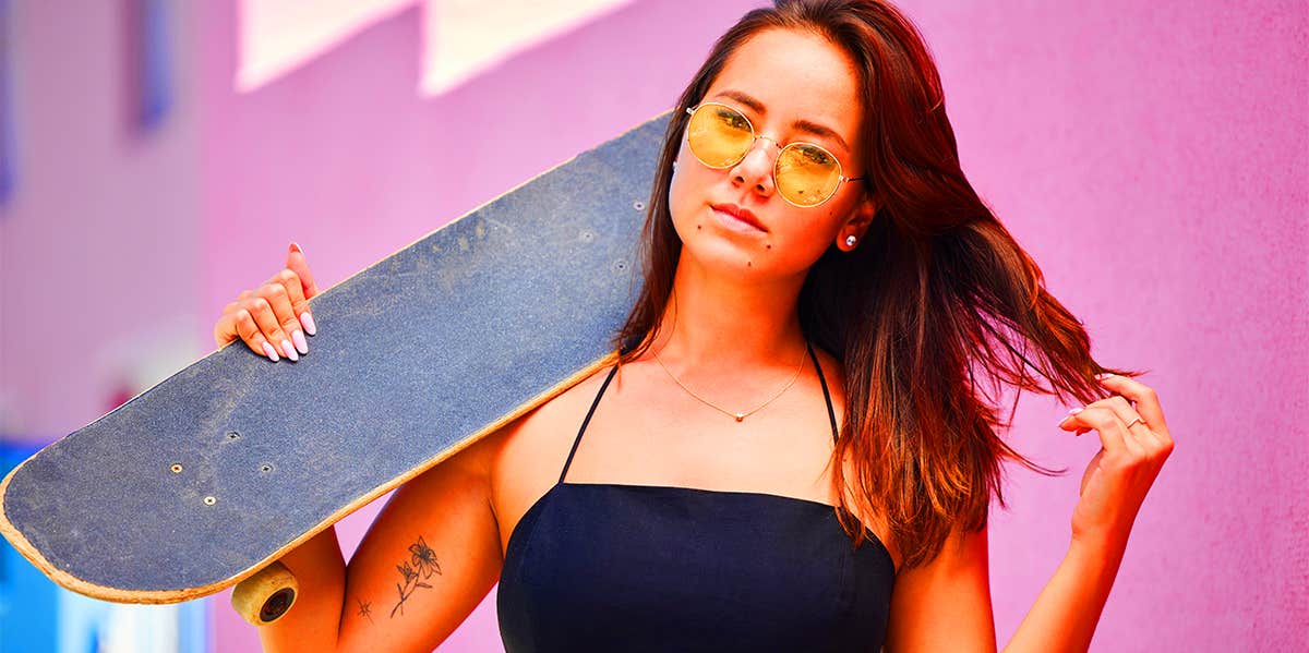 girl holding skateboard posing in front of pink wall