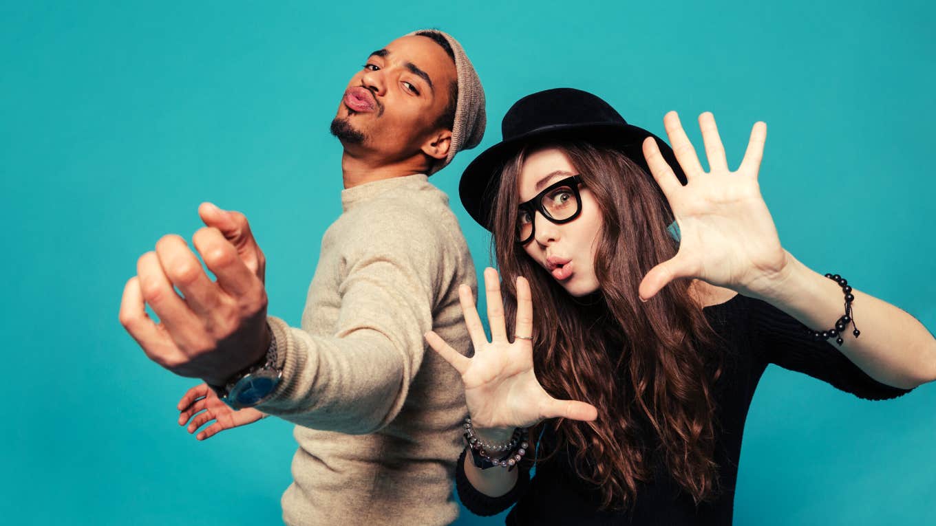 Portrait of a funny young modern couple dancing and having fun together over blue background