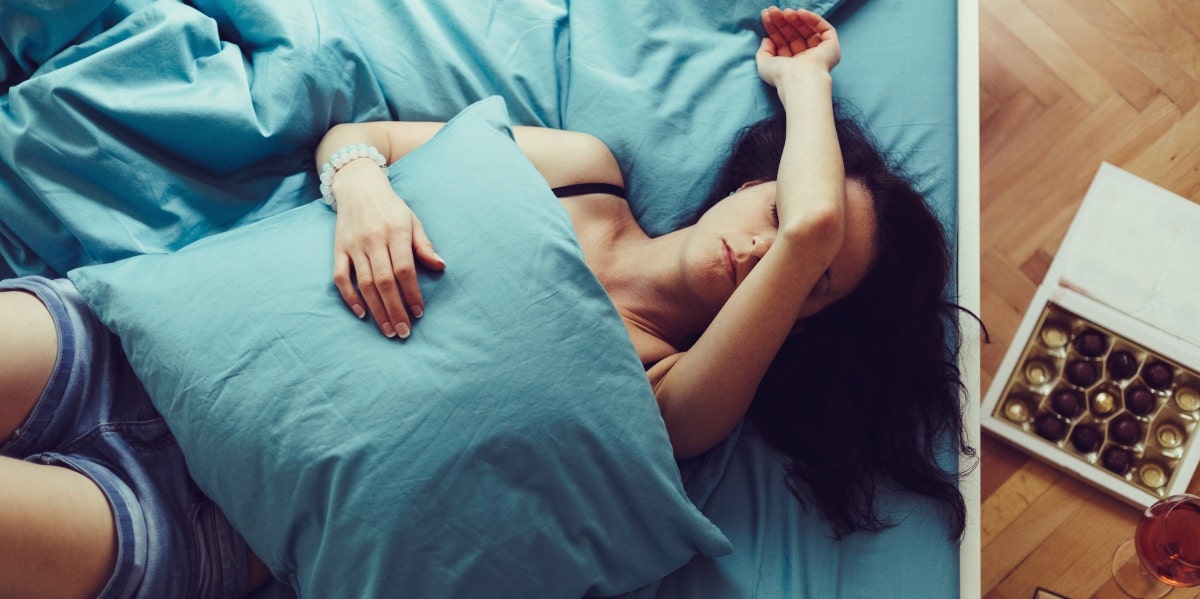 woman laying on a bed with her arm over her face holding a pillow