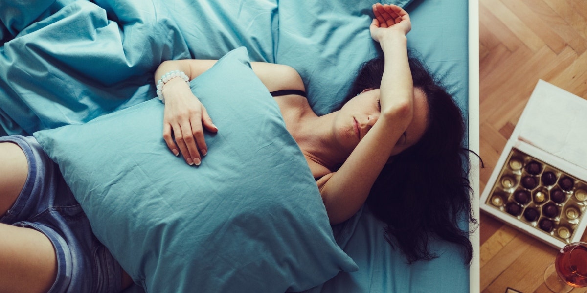 10 Reasons You Keep Dreaming About An Ex, According To An Expert woman laying on a bed with her arm over her face holding a pillow