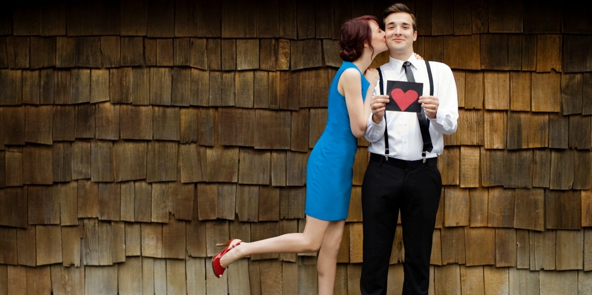 man holding a drawing of a heart while woman kisses his cheek