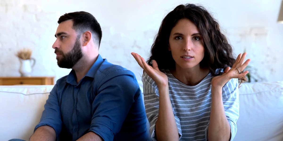 A woman looks at the camera in frustration as her spouse looks away behind her