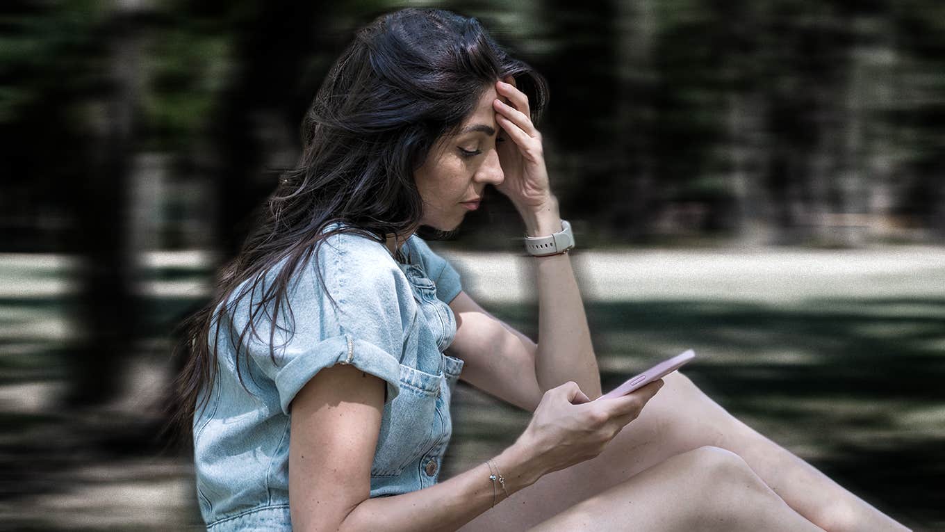 sad woman sitting in park looking at phone