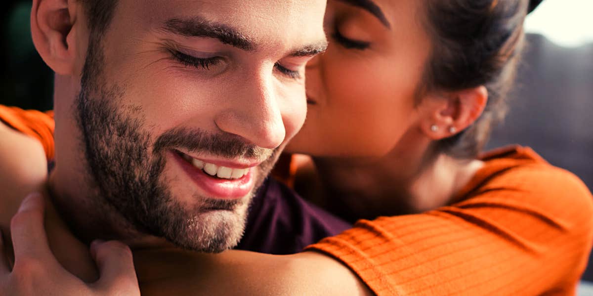 woman hugging smiling man from behind and whispering in his ear