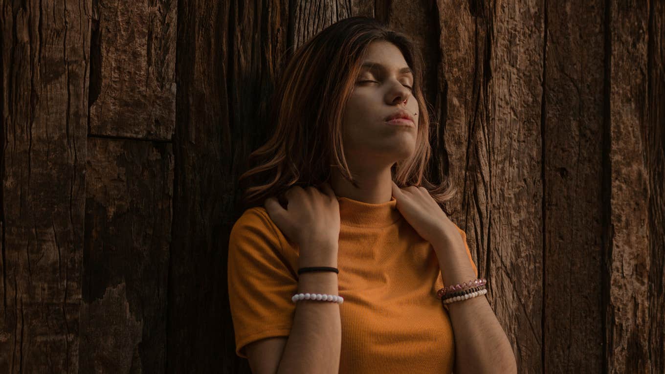 Woman in Orange Turtleneck Shirt Leaning on Brown Wooden Wall