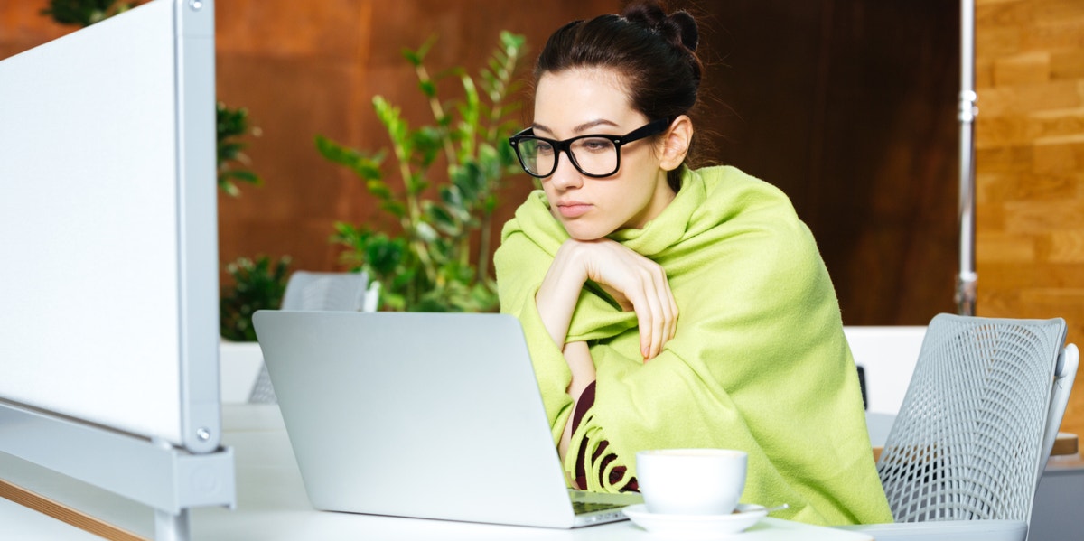 Why Women Are Always Freezing At The Office, According To Studies woman working in blanket