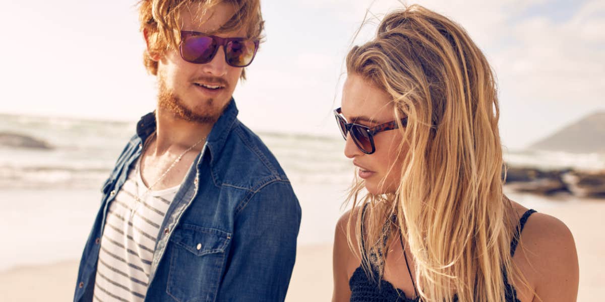 man and woman walking on the beach, she looks disinterested