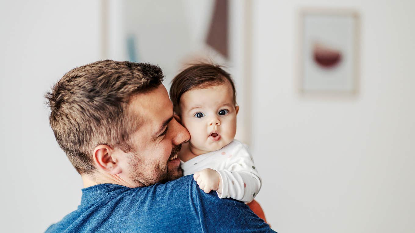 baby girl in father's arms looking at the camera.