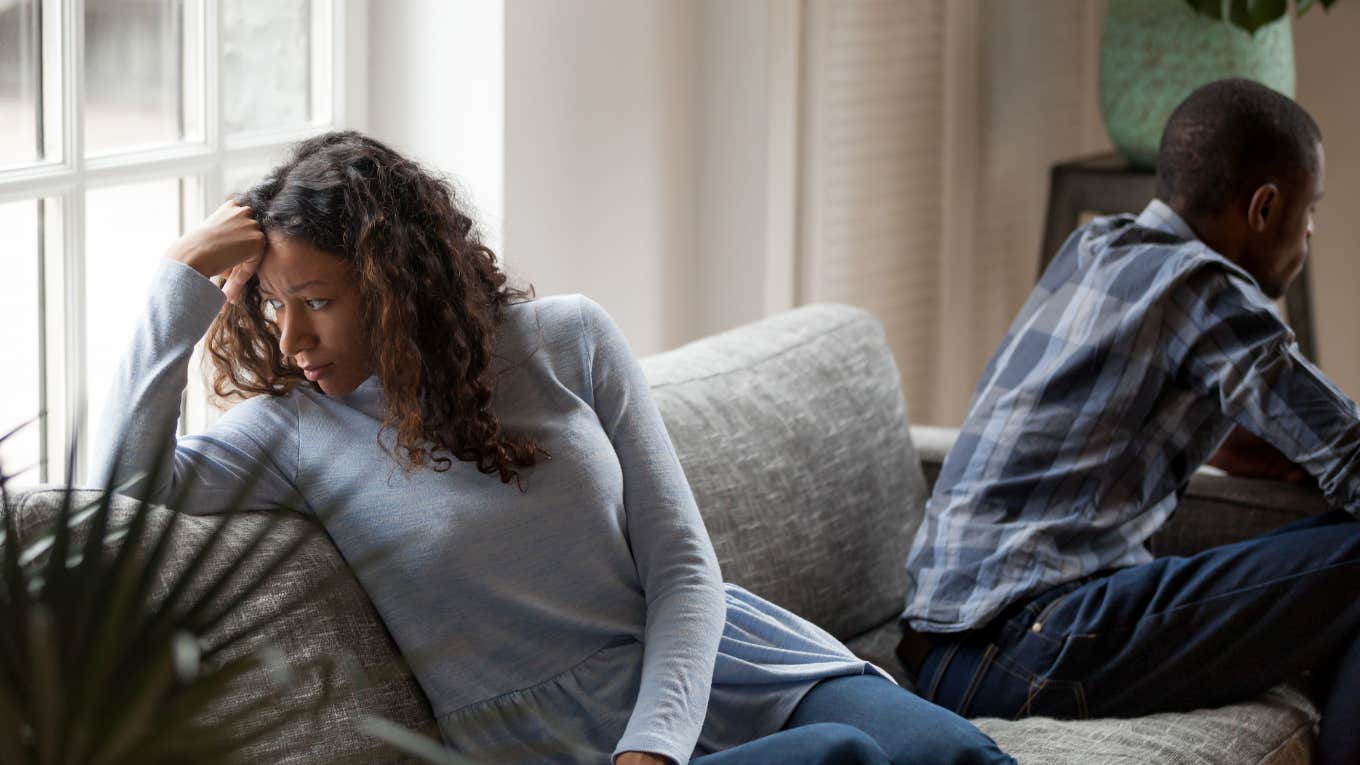 upset couple sitting far apart from each other on a couch with their backs turned to each other