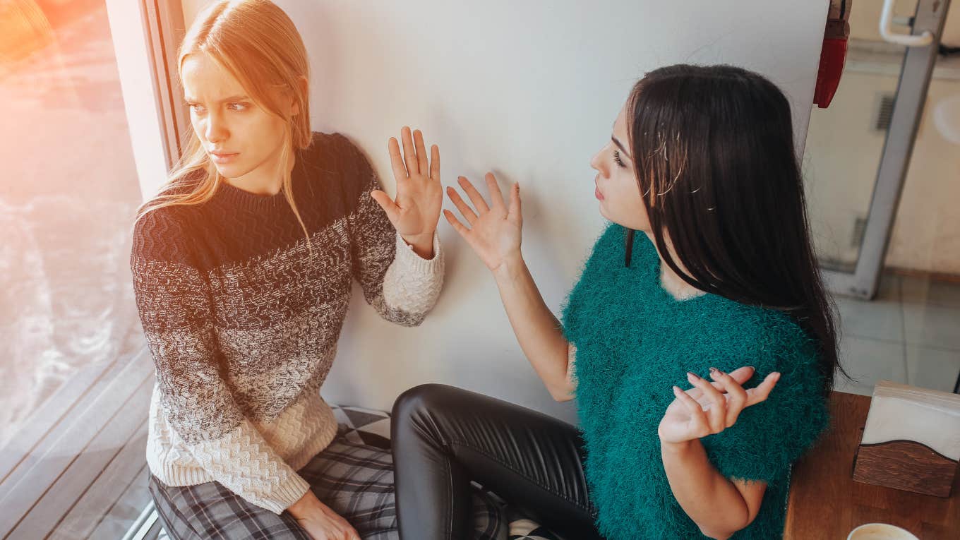 woman holding up hand at other women while the two argue