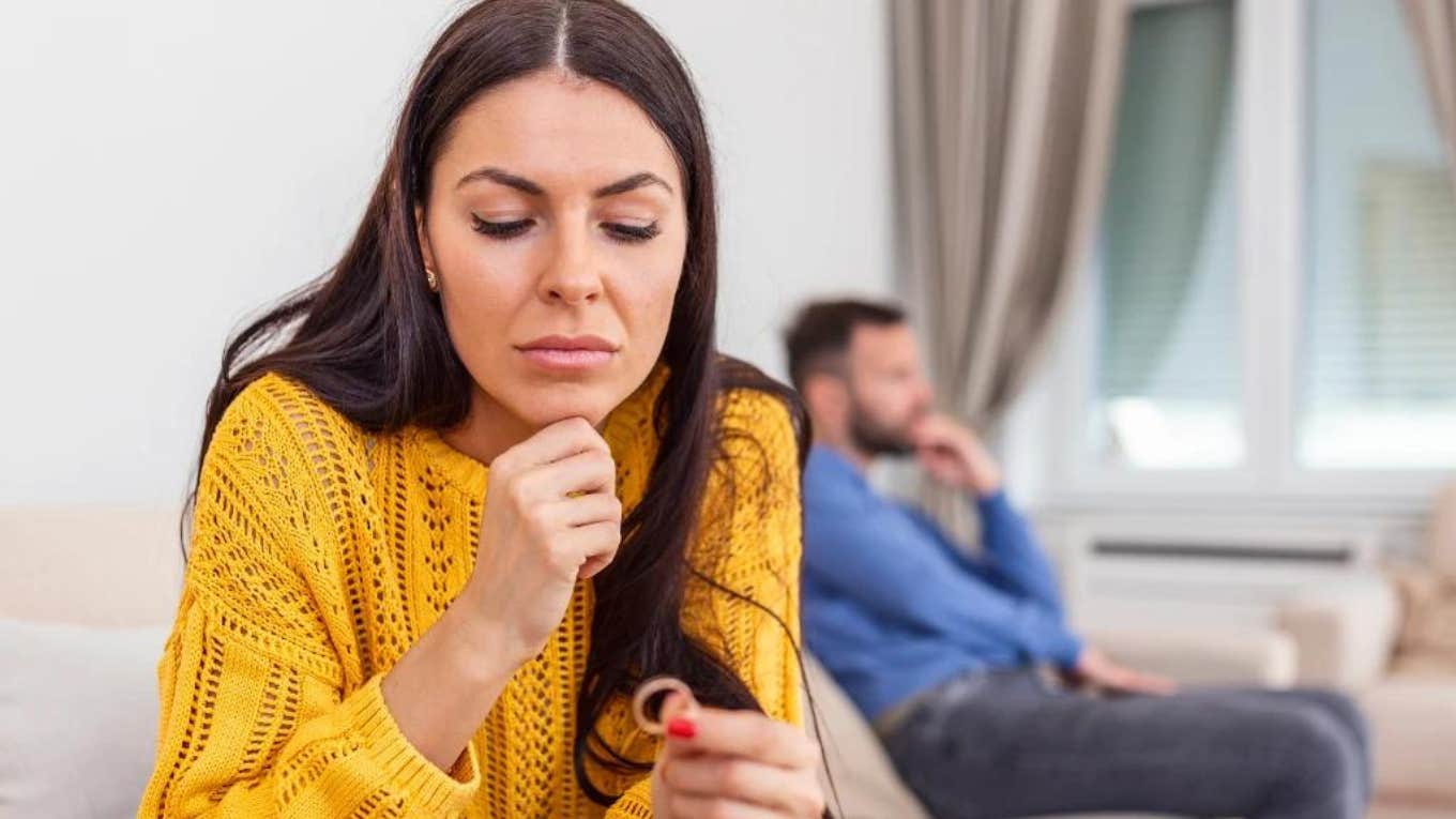 Woman looking at her wedding ring husband in background