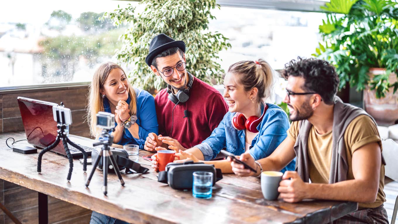 young people laughing and sitting at table in front of phone cameras