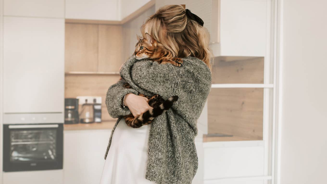 Woman hugging her cat in her kitchen. 