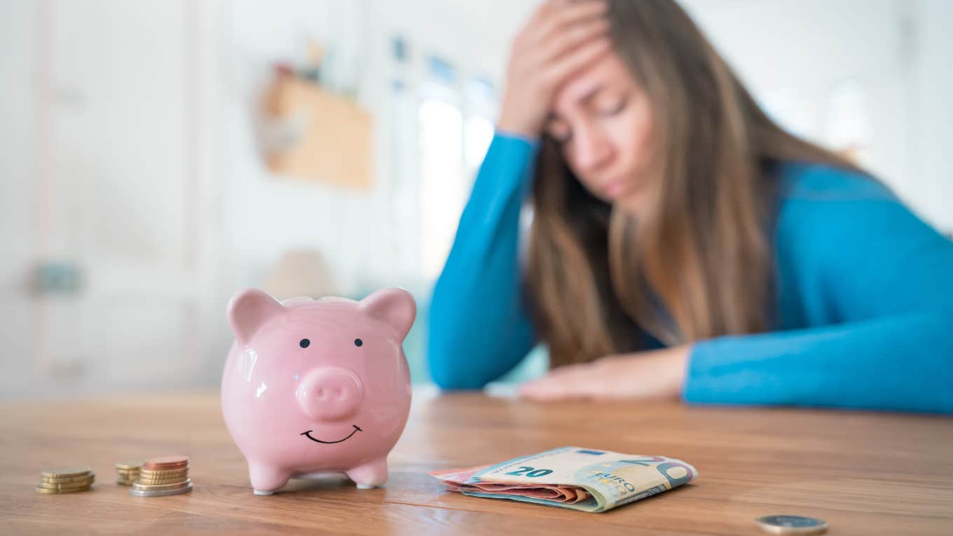 frustrated woman sitting at table with money and piggy bank