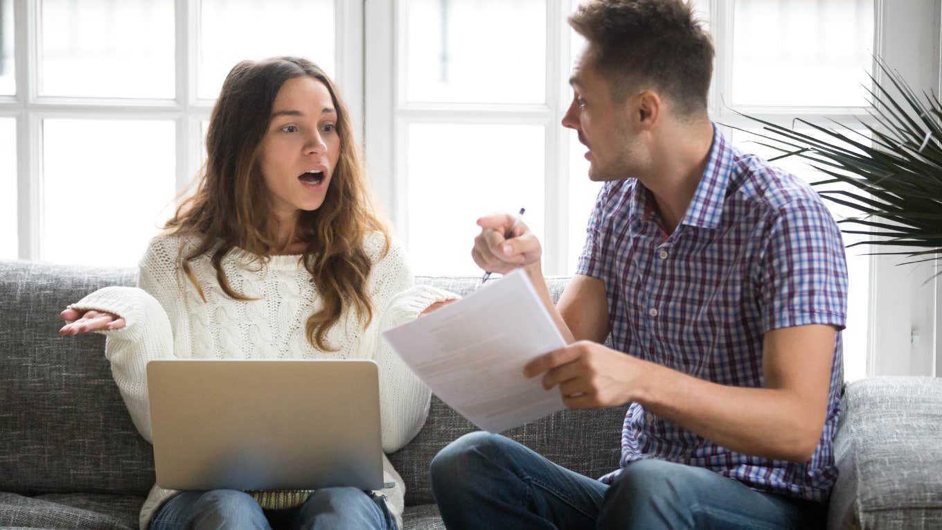 unhappy couple arguing while sitting on couch in front of laptop and papers