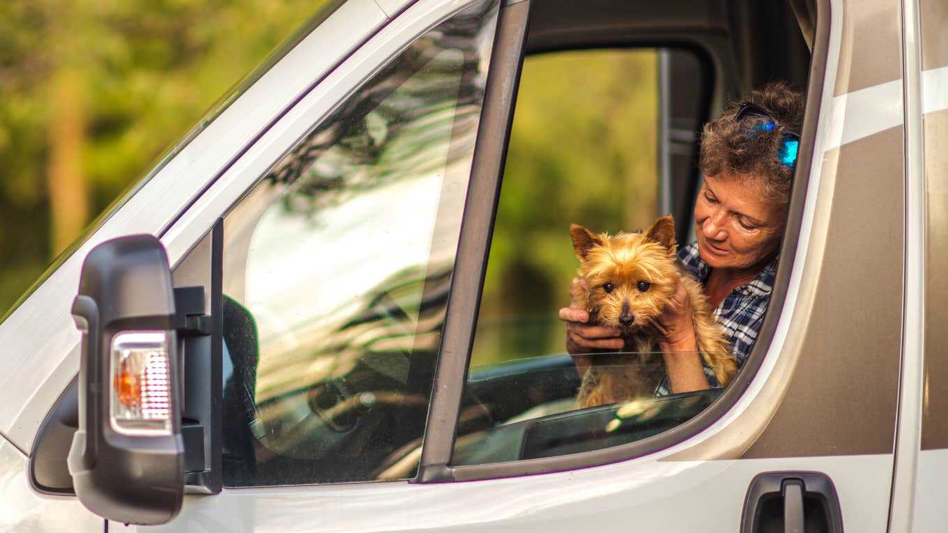 Woman holds her dog in a car window. 