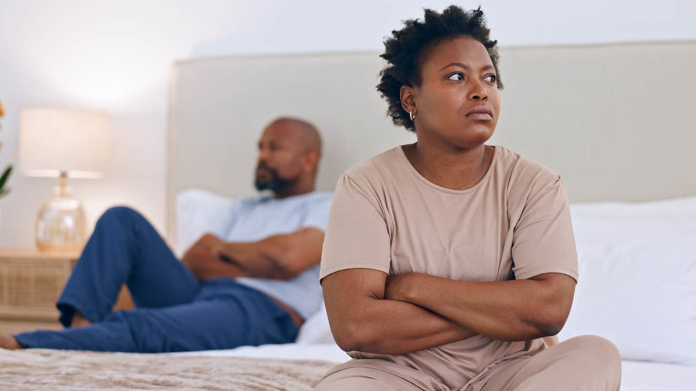 Woman sits at the edge of her bed, facing away from her husband. 