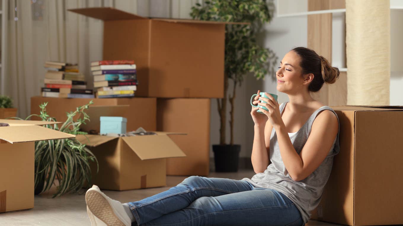 woman sitting on floor with coffee mug in hand surrounded by moving boxes