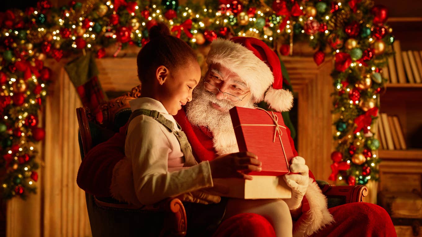 girl opening Christmas present while sitting on Santa's lap