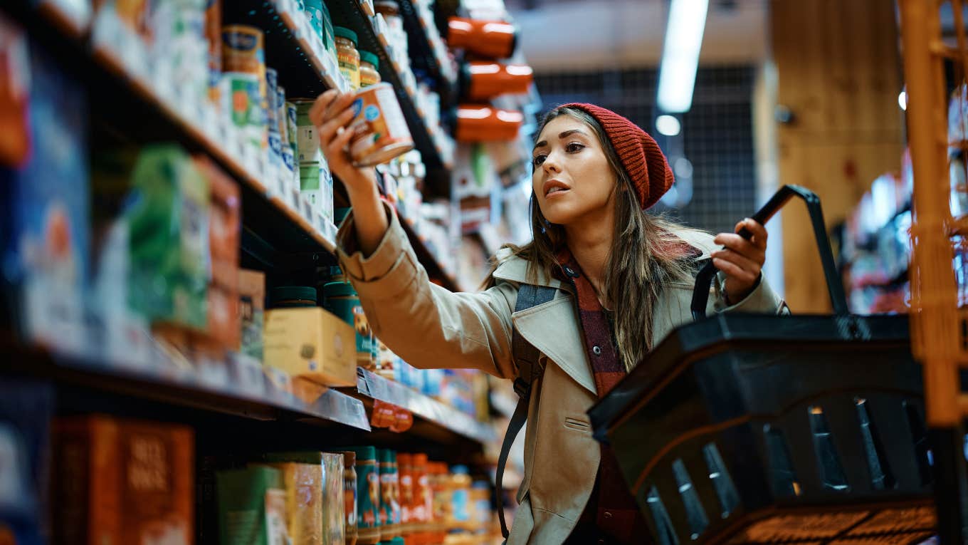Young woman buying canned food at grocery store.