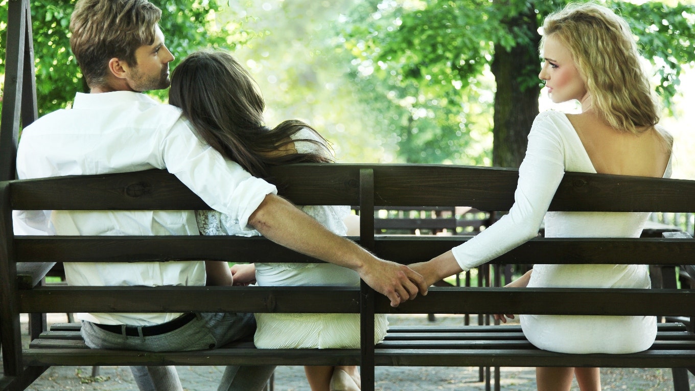 A woman is holding a man's friend behind his partner's back.