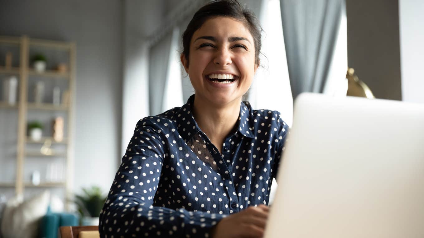 woman sitting at desk with laptop laughing