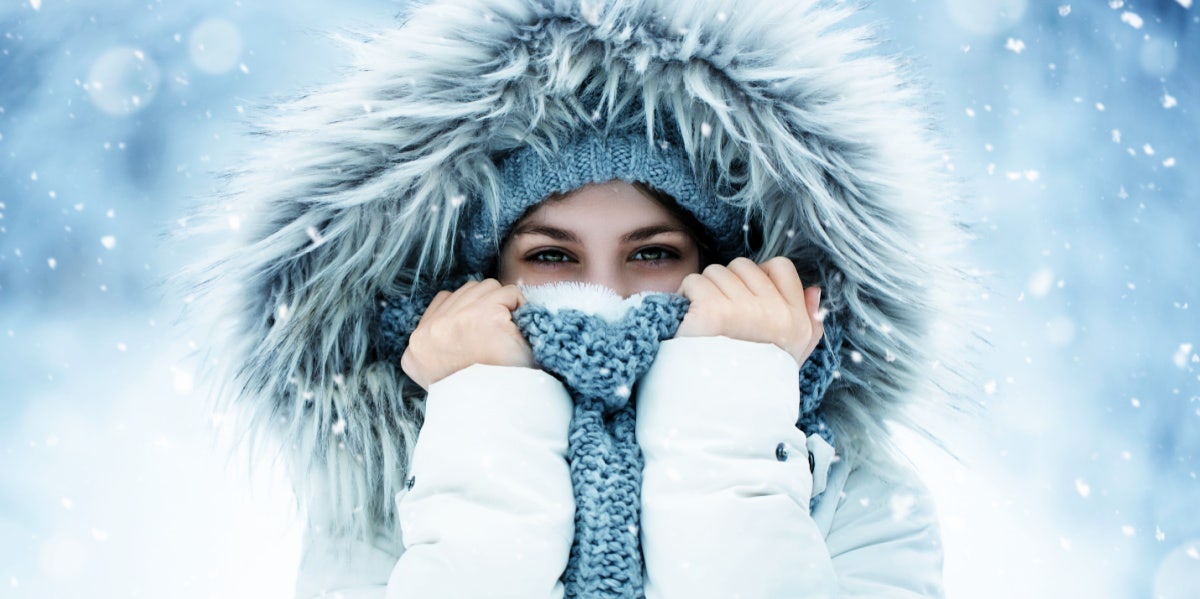 woman stands in the snow wearing a fur hood and covering her face