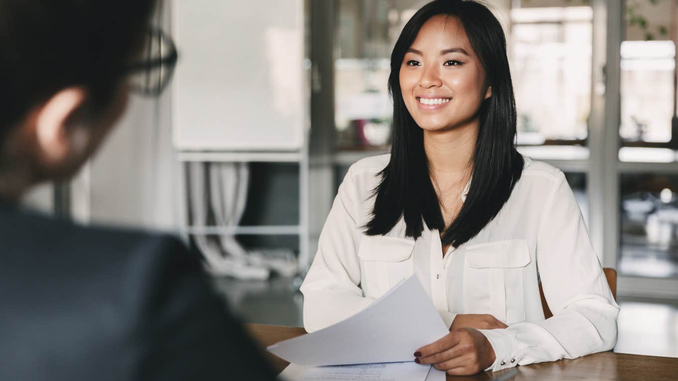 woman smiling and holding resume while sitting in front of businesswoman during corporate meeting or job interview