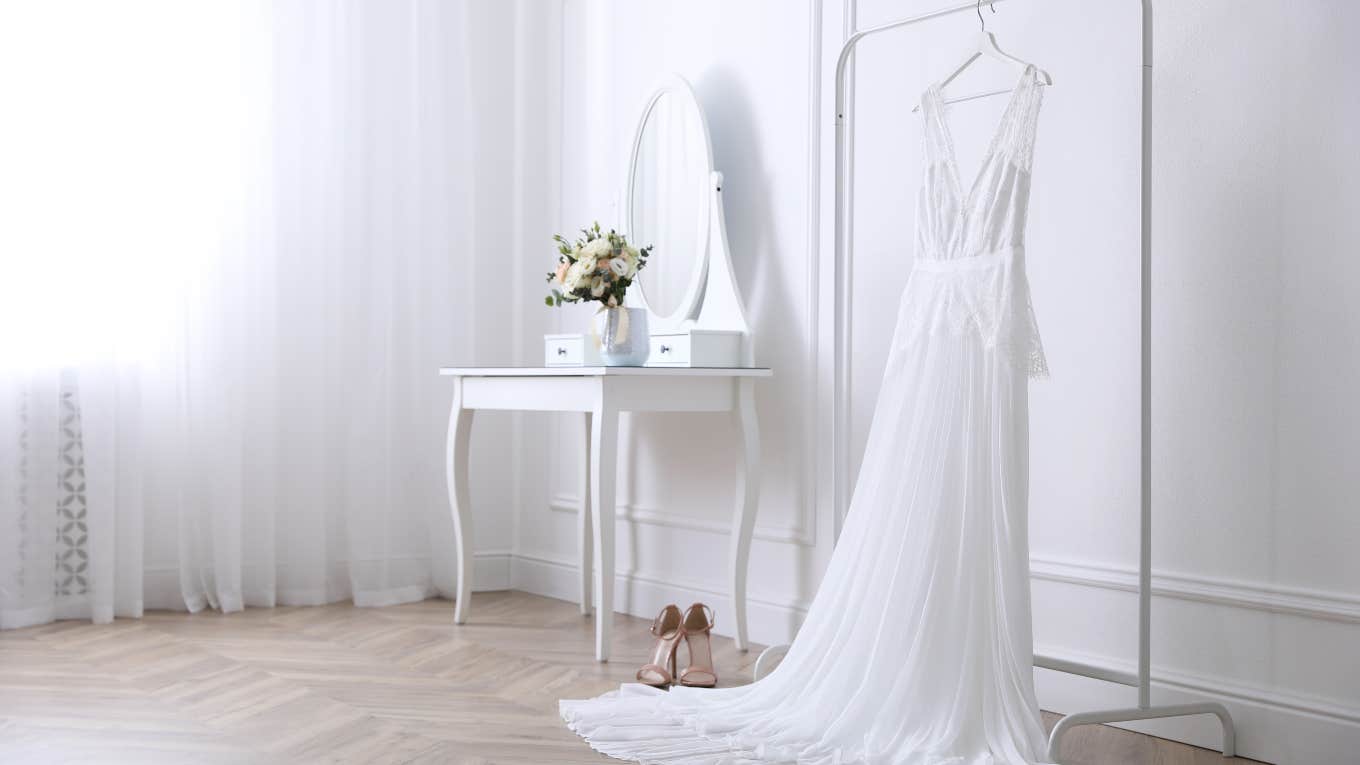wedding dress hanging on clothing rack with vanity and flowers in background
