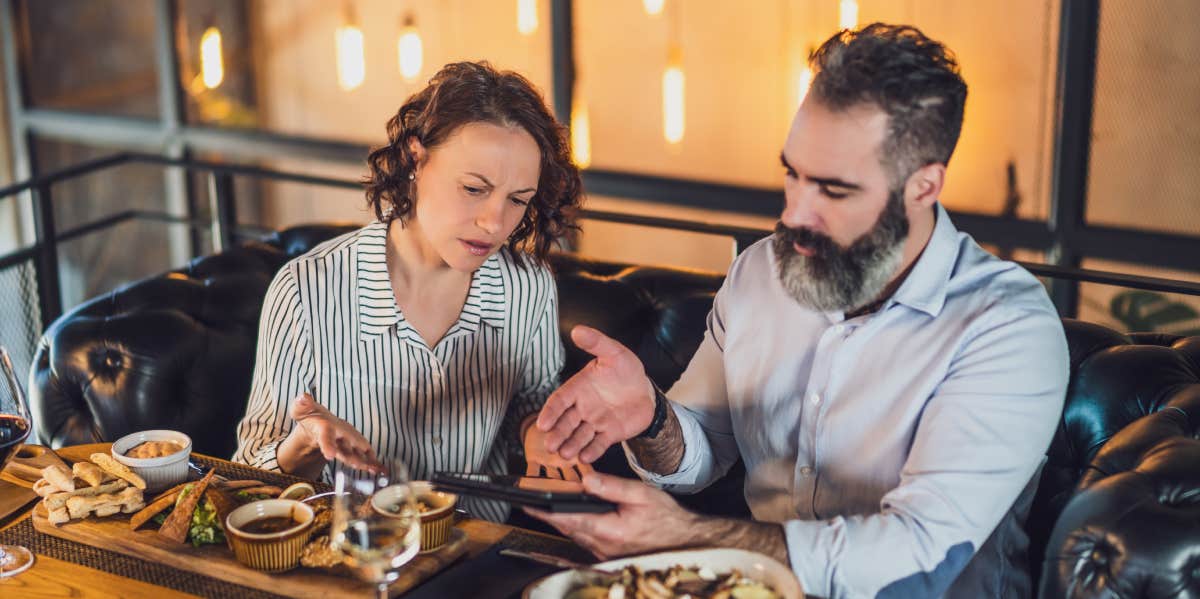 couple sitting at restaurant arguing over bill on tablet