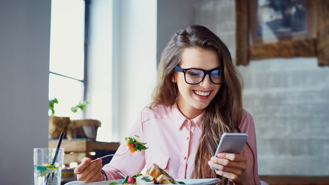 woman sitting at restaurant eating salad while looking at phone