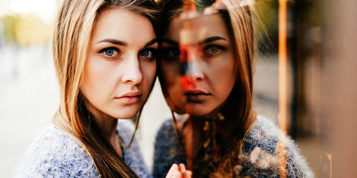 serious woman leans against a mirror