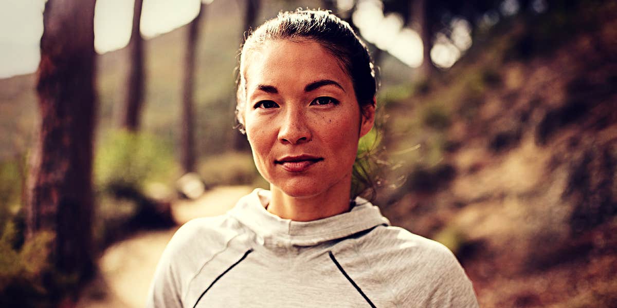 Women can balance their hormones by managing stress Asian woman standing in the woods wearing a running hoodie