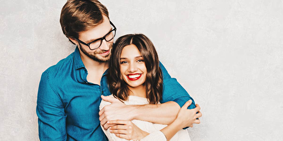 Women who find true love man and woman embrace, him behind her, against a concrete wall
