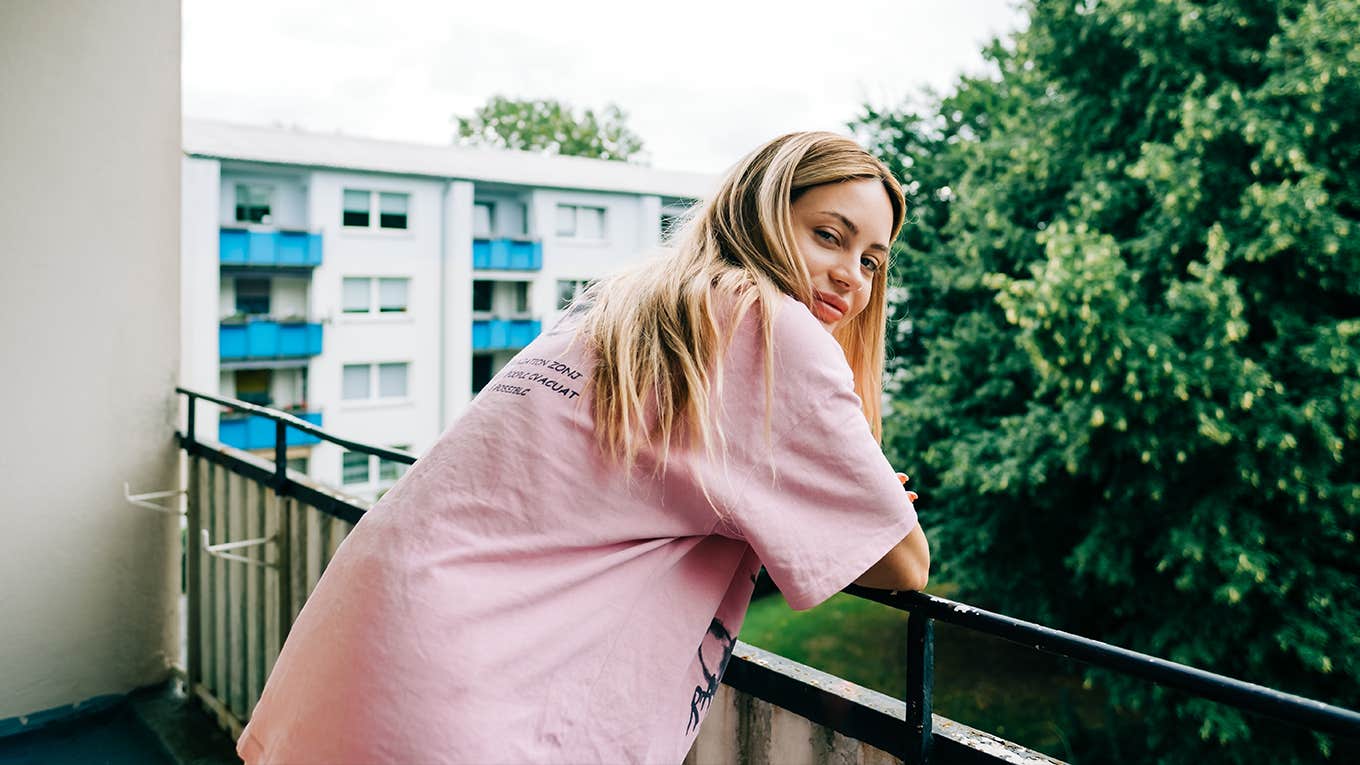 Young caucasian woman staying on loggia balcony and looks around.