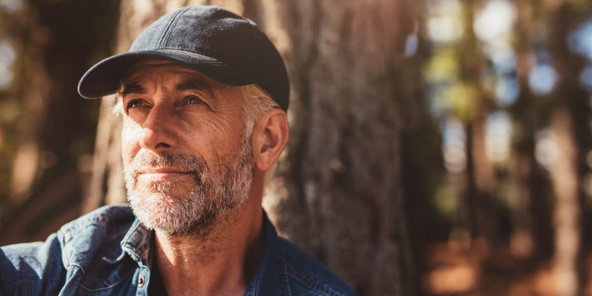 handsome man in his sixties, grey beard, in the woods